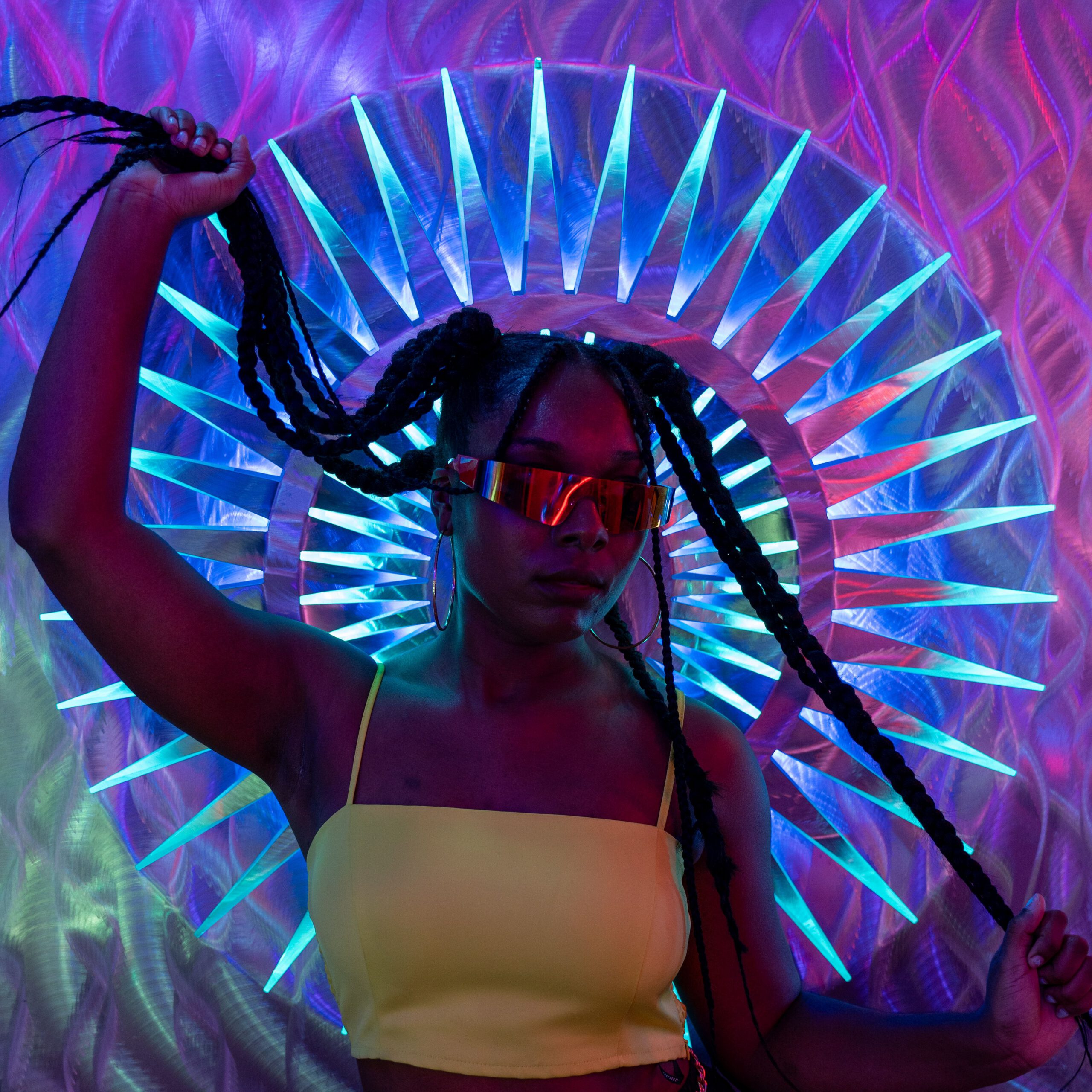 A stylish woman with braids and sunglasses in a neon-lit club setting.