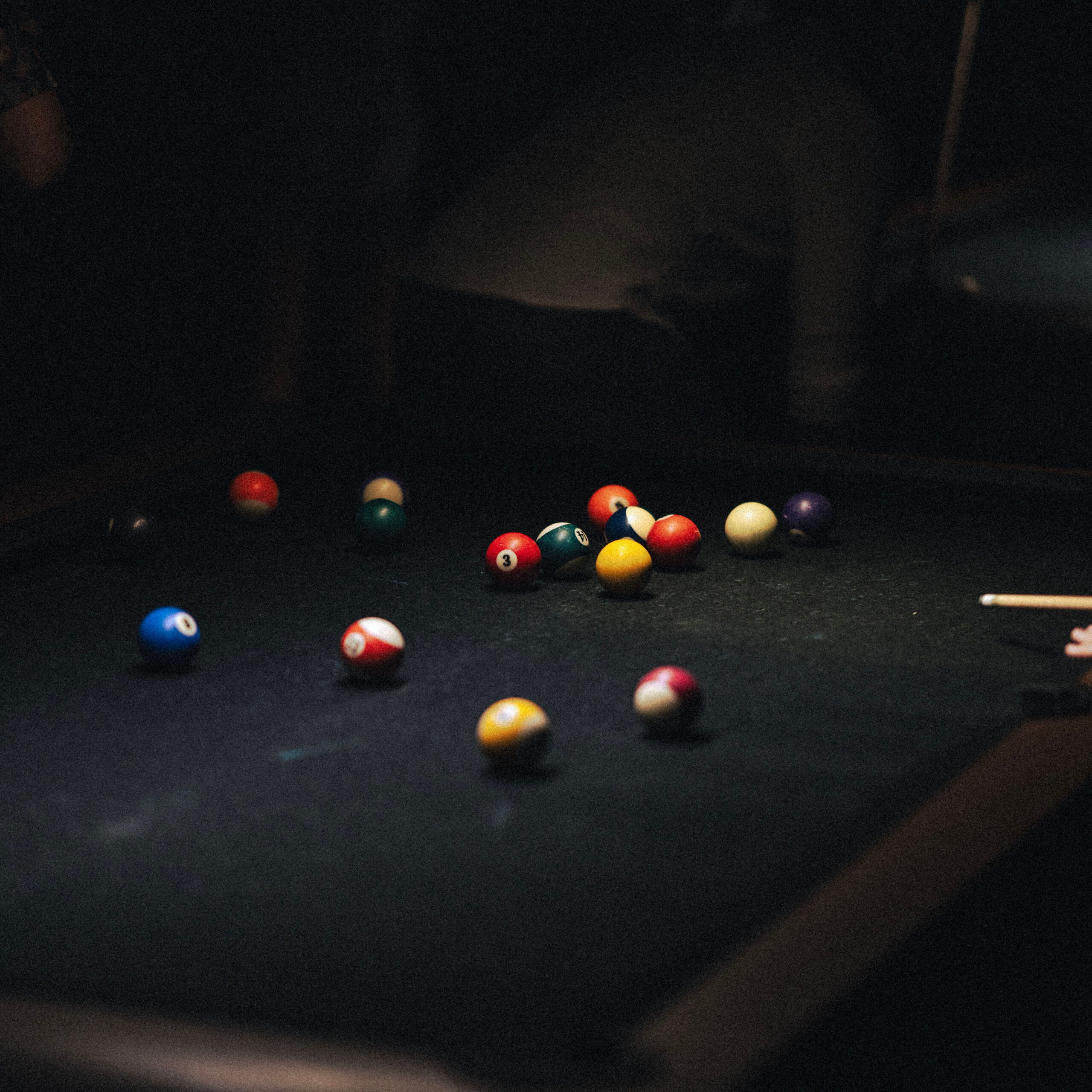 Colorful billiard balls on table in dimly lit room, capturing the intense mood of a game in progress.