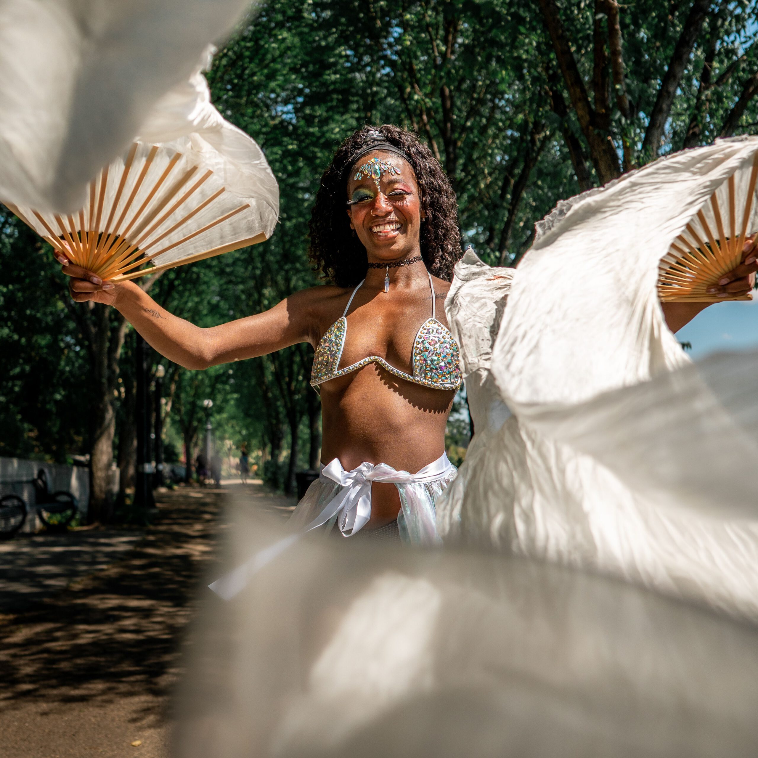 A joyful performer dancing outdoors with white fabric fans, radiating happiness and energy.